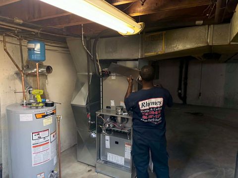 Technician inspecting a furnace and water heater in a basement utility room