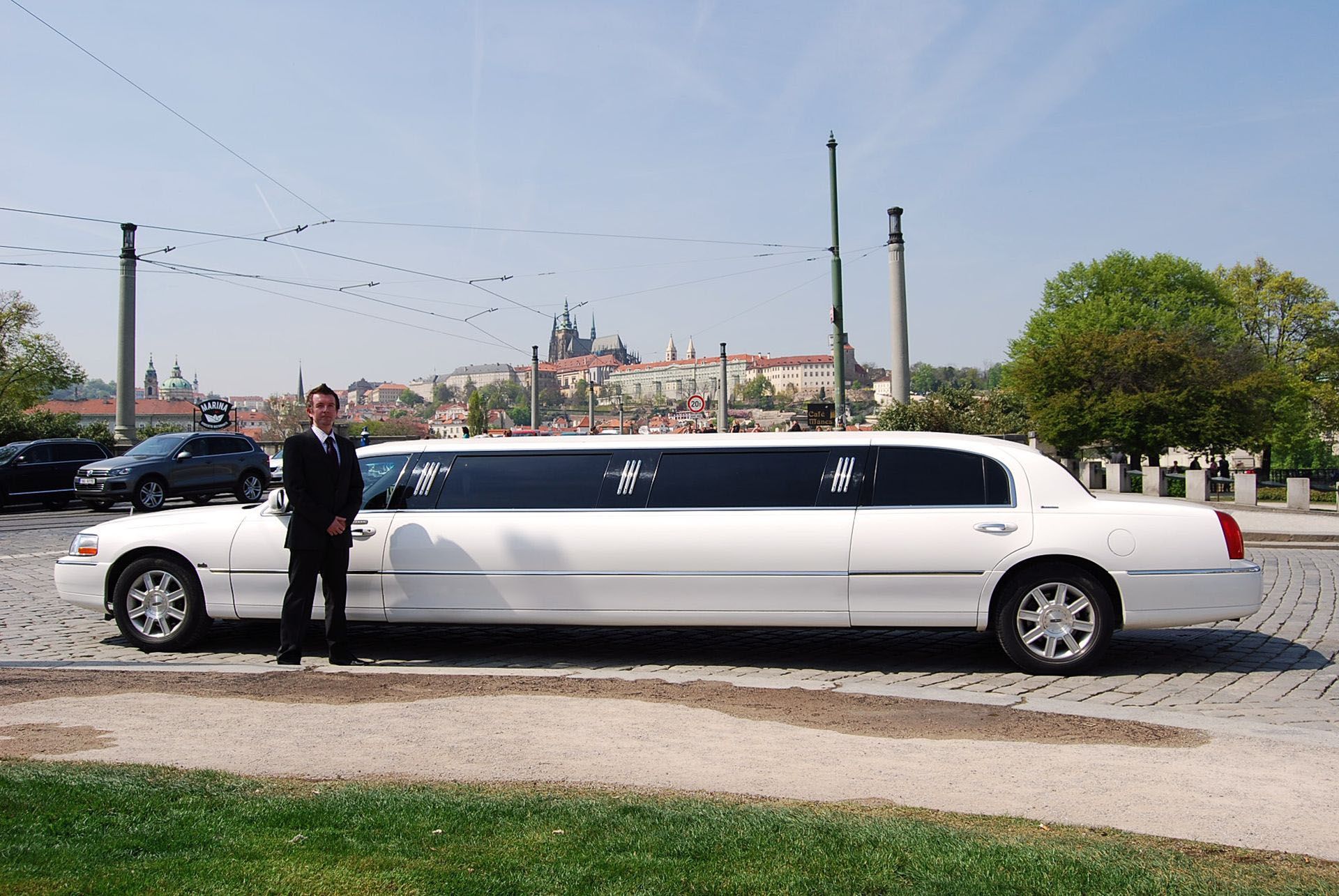 A man in a suit is standing next to a white limousine.