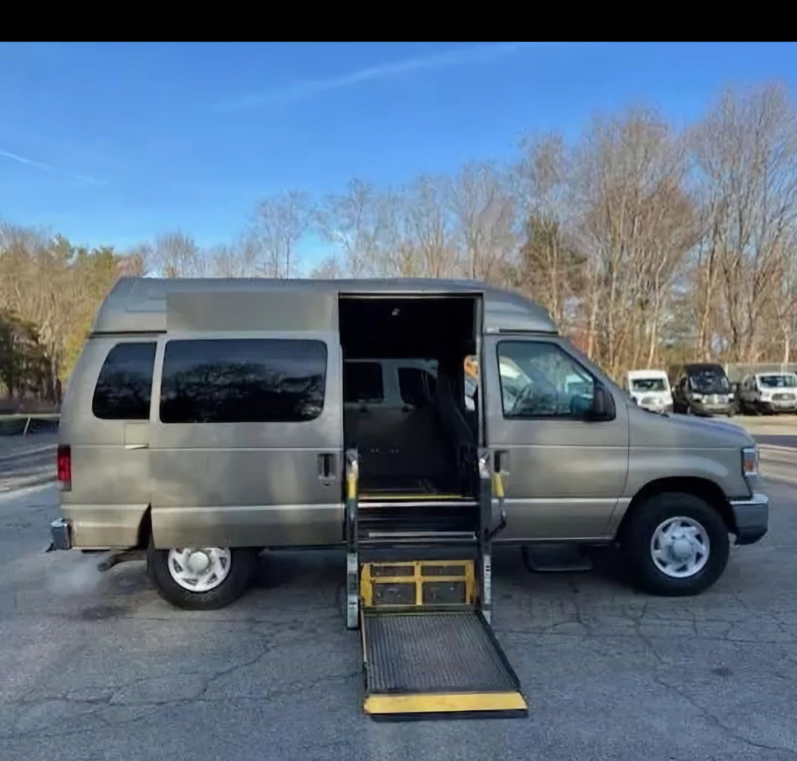 A gold Ford passenger van with a side-entry wheelchair lift deployed in a parking lot.