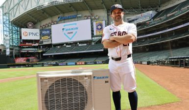 Baseball player with arms crossed, next to an air conditioning unit, at a stadium.