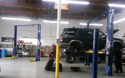 Car repair shop with a vehicle on a lift, mechanic working. Tools and equipment visible.