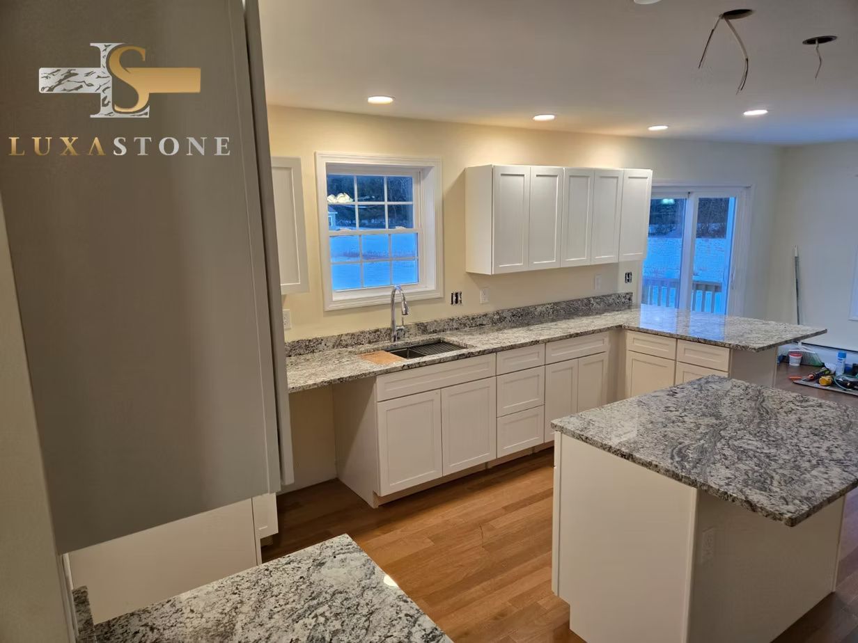 A kitchen with white cabinets and granite countertops. A sink and two islands are visible.