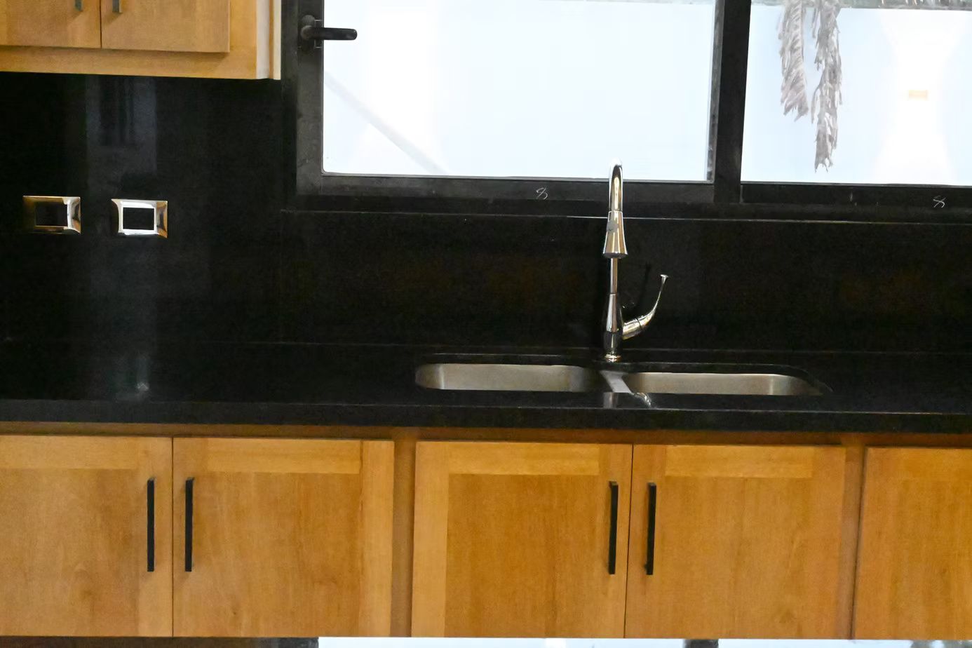 Kitchen sink with black countertop, light wood cabinets, and a window.