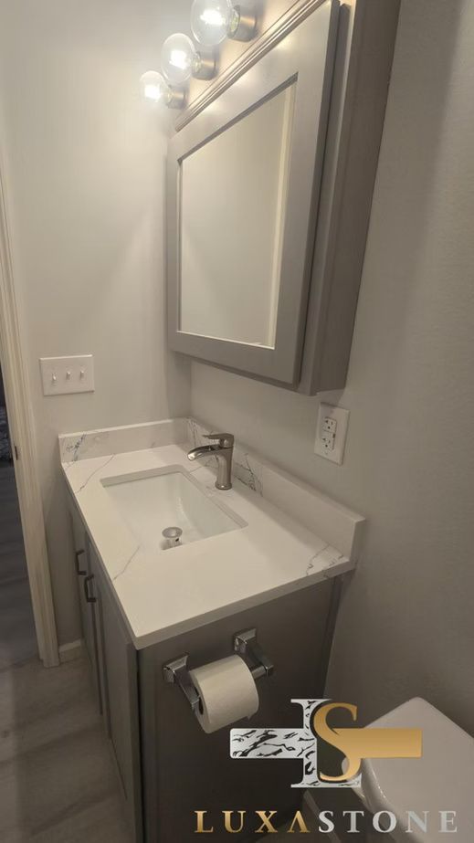Gray bathroom vanity with quartz countertop, mirror, and toilet.