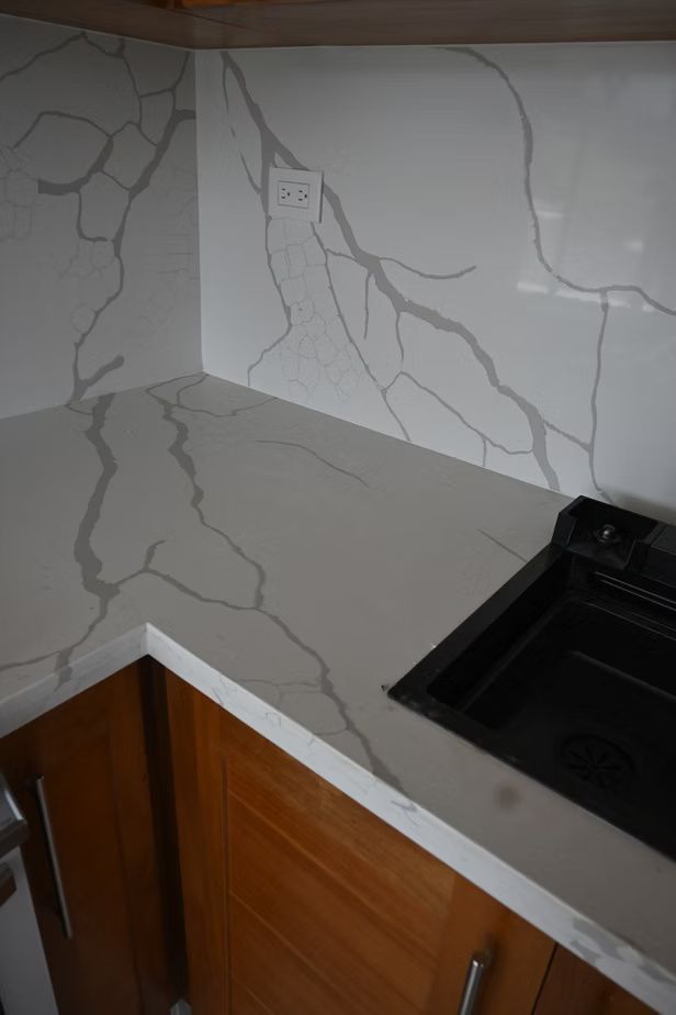 Kitchen countertop and backsplash with gray veining, next to a stovetop and wooden cabinets.