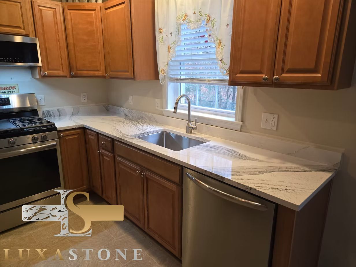 Kitchen with light-colored countertops, brown cabinets, stainless steel appliances, and a window with a curtain.