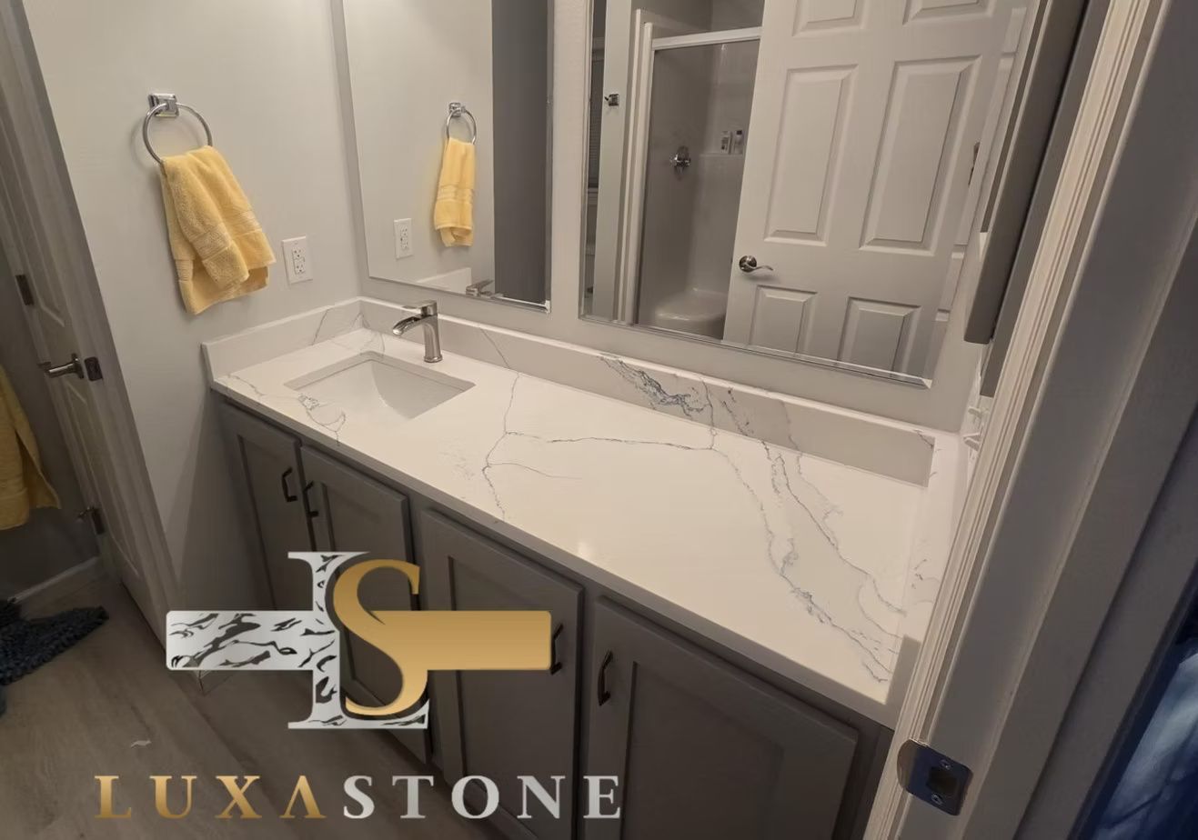 A bathroom vanity with white countertop and gray cabinets. A mirror reflects the shower, a yellow towel hangs.