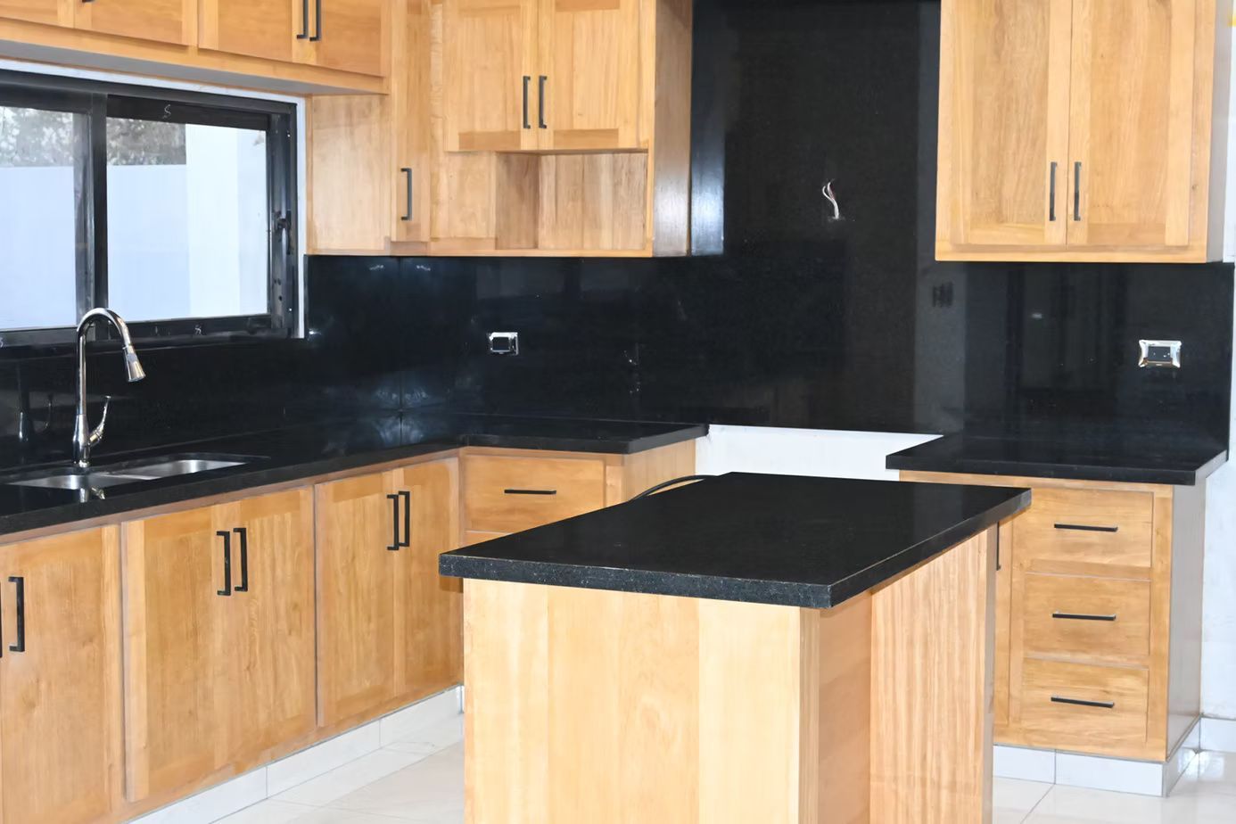 Kitchen with light wood cabinets, black countertops, and a black backsplash.