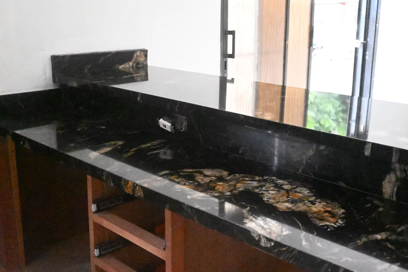 Black granite countertop with wooden cabinets, near a window.
