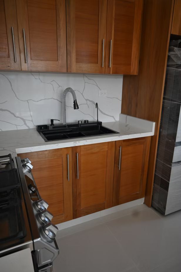 Wooden kitchen cabinets with a black sink, white countertop, and marble backsplash.