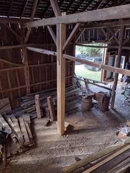 Interior view of a rustic wooden barn with exposed beams and a central support post, looking out toward a grassy yard.