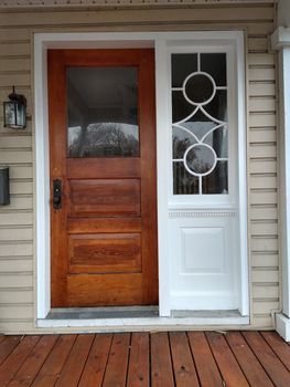 A wooden front door with a glass pane next to a white side panel featuring a decorative geometric window design.