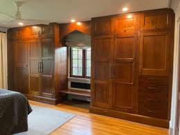Large wooden wardrobes flank a central recessed window and bench in a bedroom with hardwood floors.