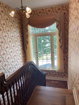 A room with pale green patterned wallpaper, a fireplace, dark green curtains over a window, and a patterned carpet.