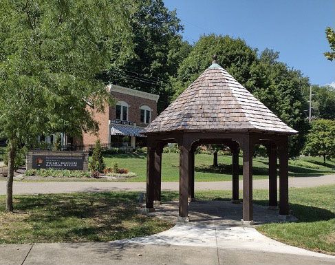 A gazebo in a park with a brick building in the background