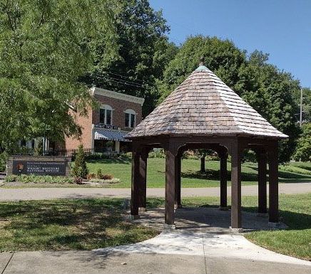 A gazebo in a park with a brick building in the background