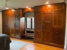 Large wooden wardrobes flank a central recessed window and bench in a bedroom with hardwood floors.