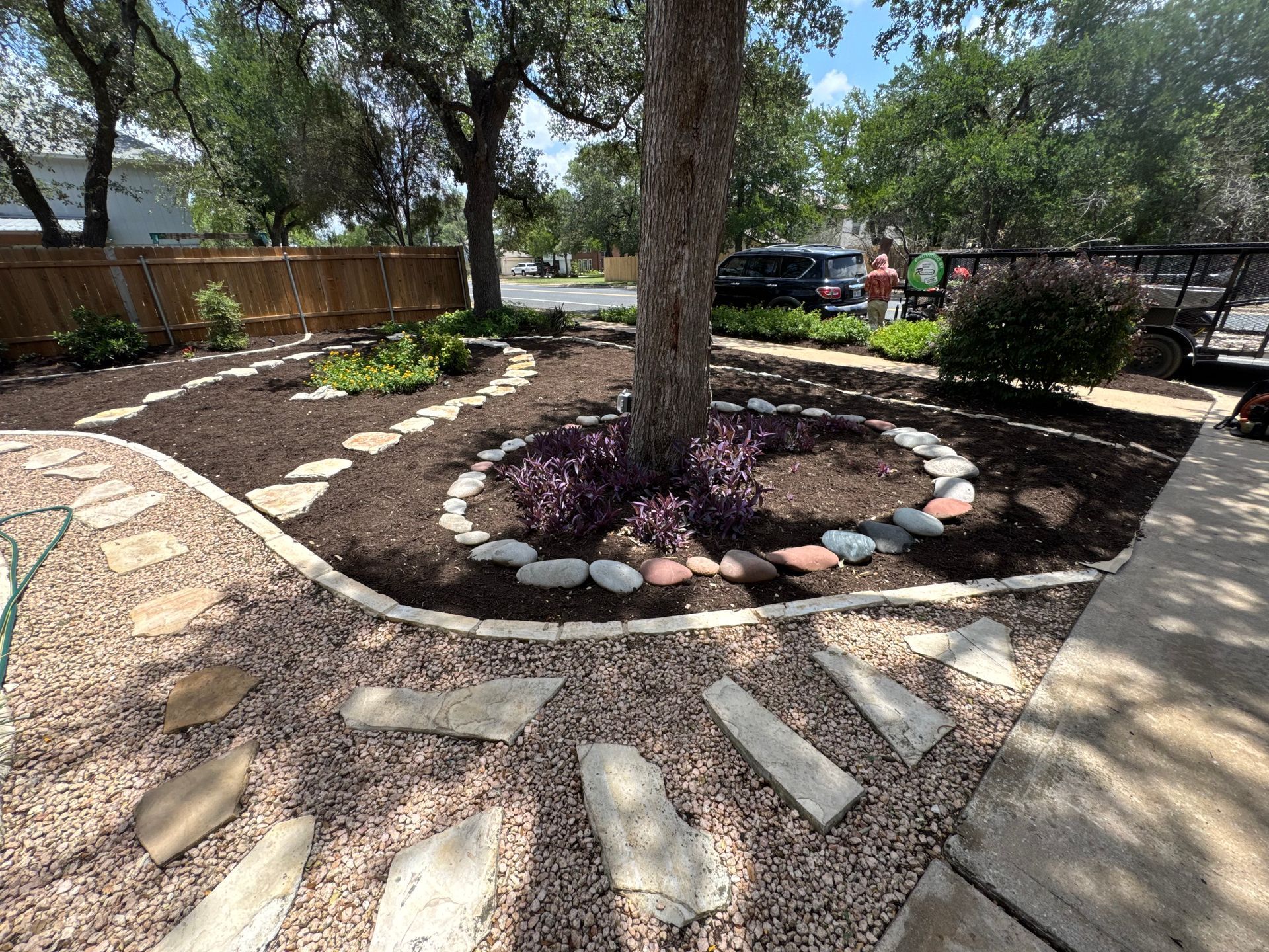 Landscaped yard with stepping stones, mulch, and plants surrounding a tree