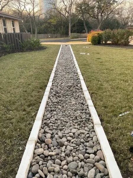 A narrow stone path bordered by concrete, running through green grass.