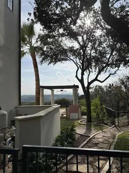 Backyard with stone path, palm tree, and covered patio with a view of the landscape under a sunny sky.
