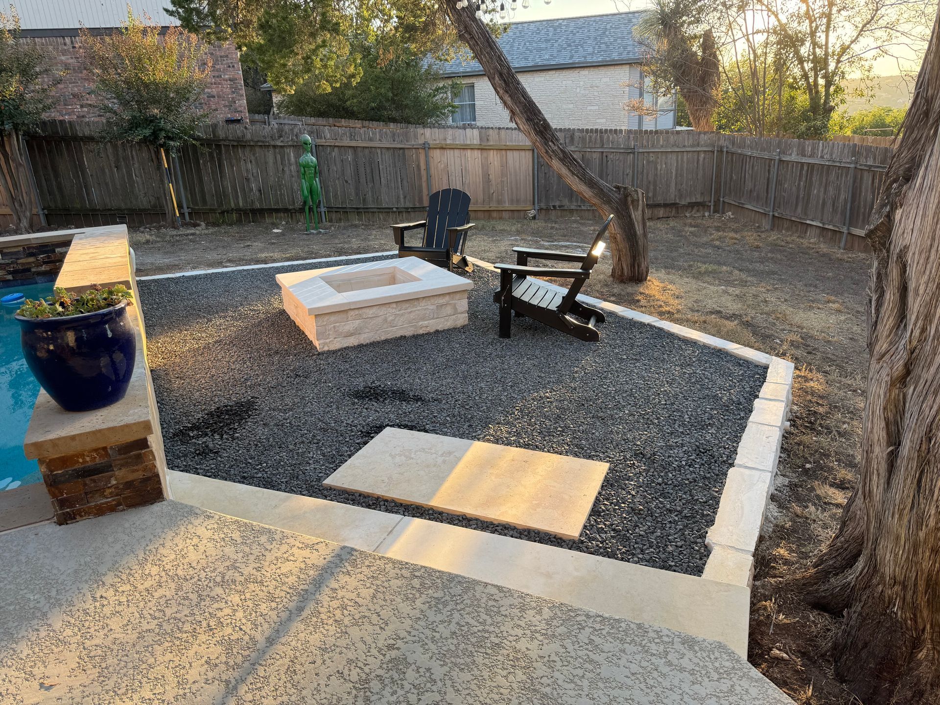 Backyard with fire pit, two chairs, and a pool. Gray gravel and a wooden fence surround the area.