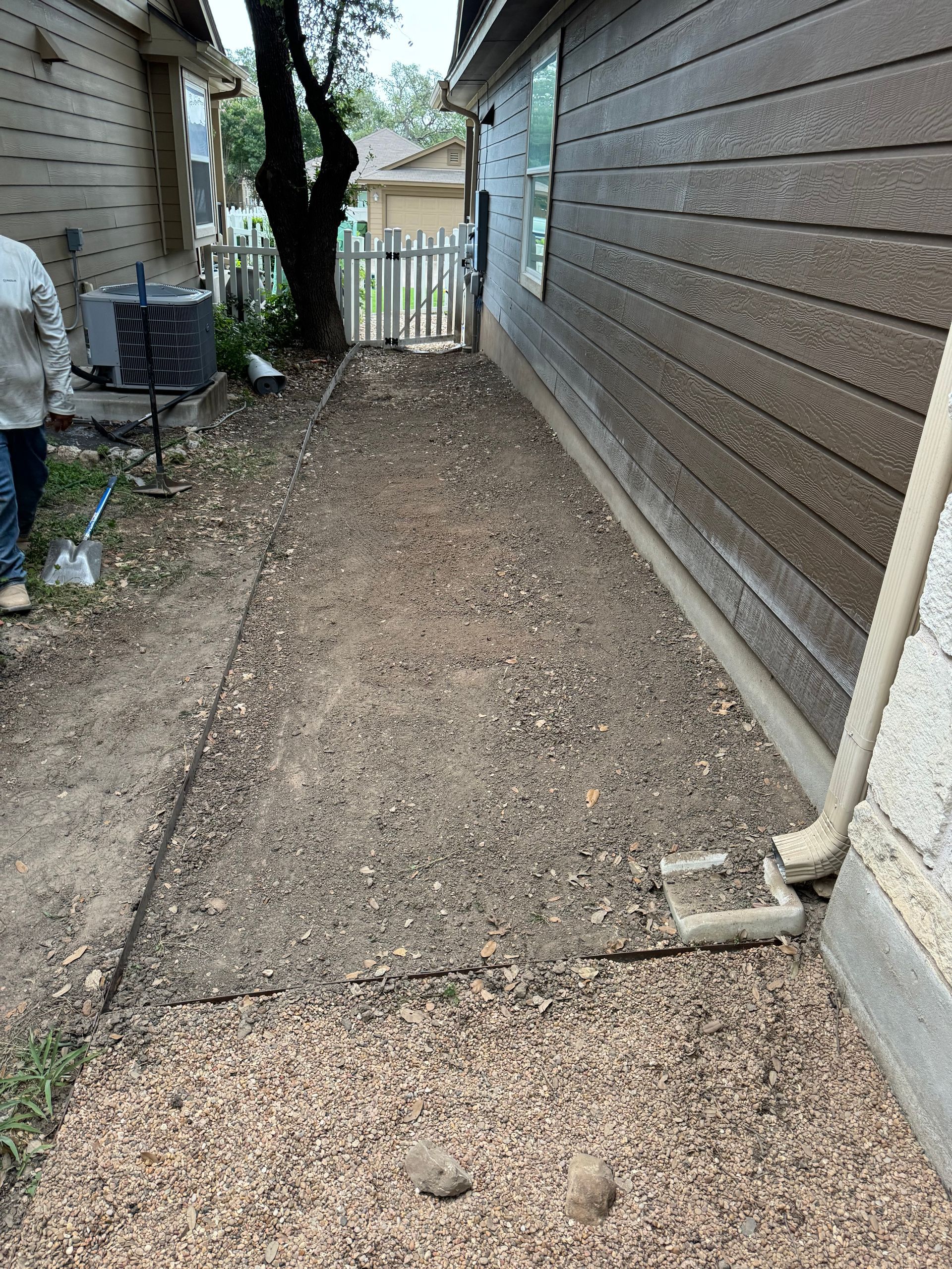 Gravel path between two buildings, leading to a white picket fence and gate.