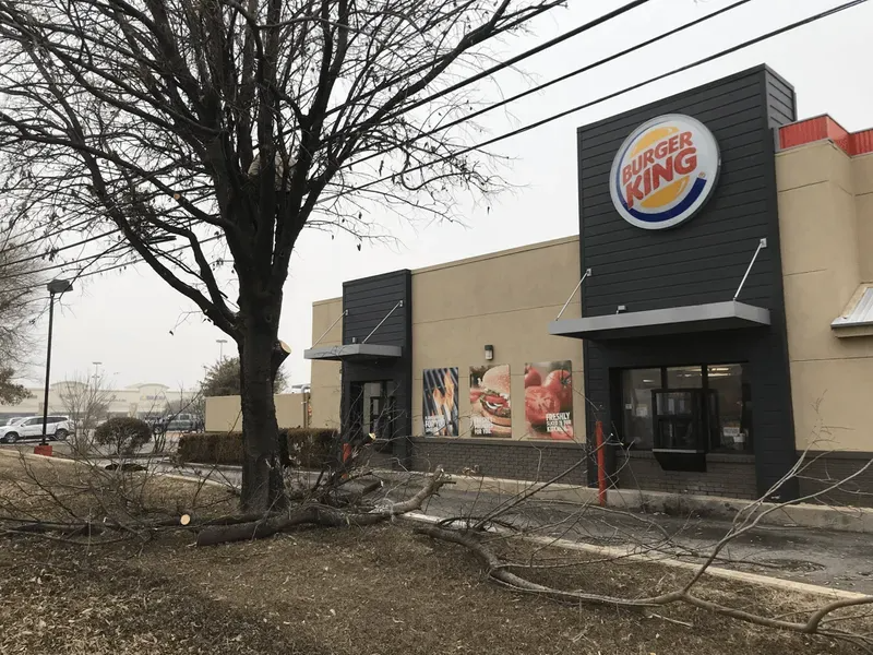 Burger King restaurant with fallen tree branches in front. Power lines visible. Overcast day.