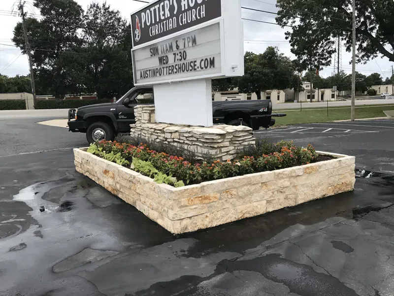Sign for Potter's House Christian Church with a stone planter box and black truck in front.