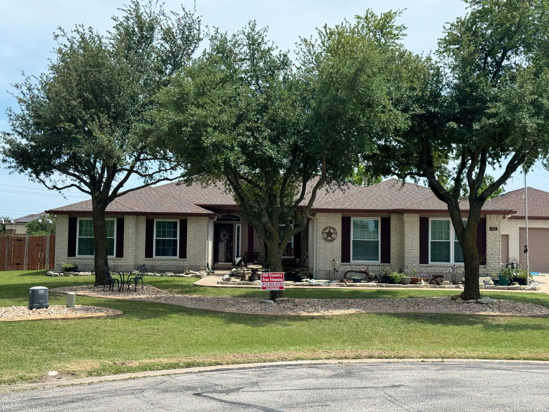 House with trees in front yard; beige brick exterior, brown roof, and for sale sign.