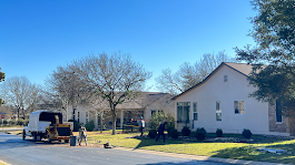 Street view of white house with construction equipment and workers on a sunny day.