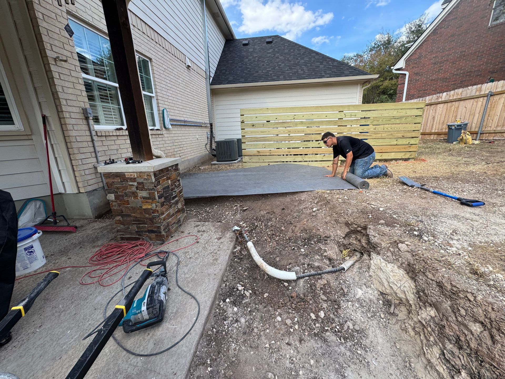 Man installing material on ground in backyard near fence and house.