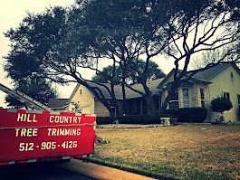 Red dumpster from Hill Country Tree Trimming in front of a house, tree branches over the roof.