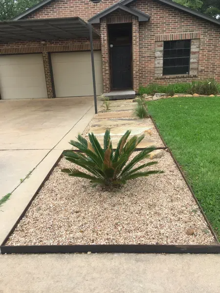 Front view of a brick house with a small gravel bed containing a cycad plant, and a concrete driveway.