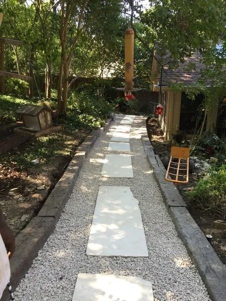 A garden path with stone slabs. Gravel borders, wooden edging. Trees and bird feeder in the background.