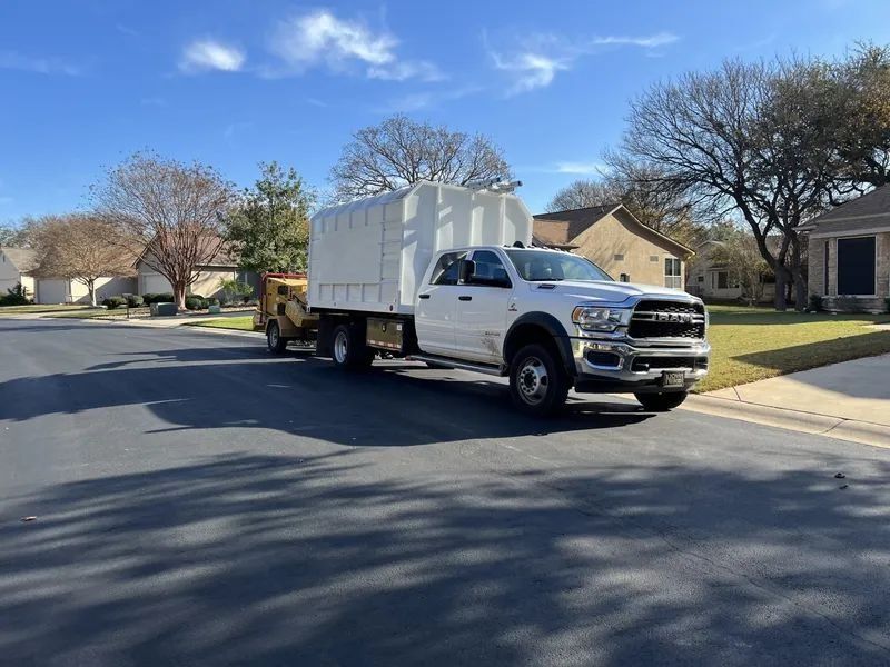 White truck towing a large white container on a residential street under a blue sky.