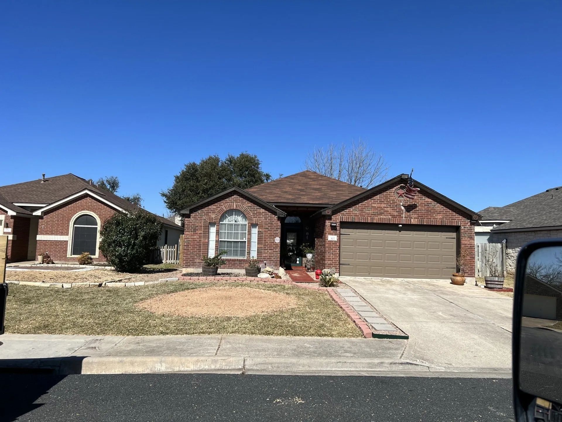 Red brick house with brown roof and garage door; blue sky.