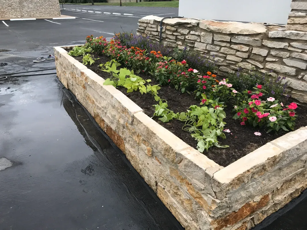 Stone planter box with colorful flowers and green plants.