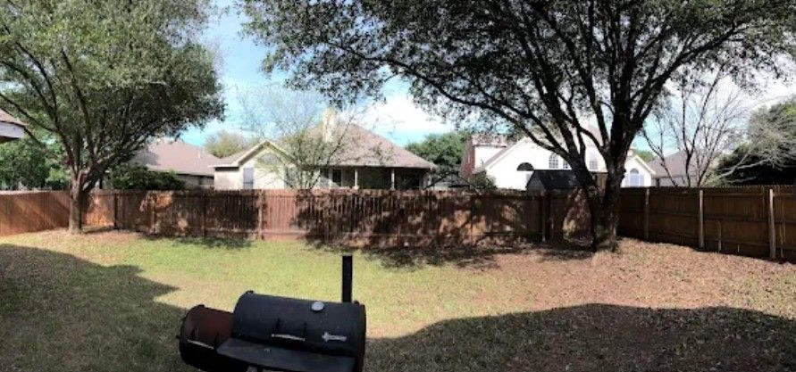 Backyard view with a smoker, wooden fence, trees, and houses.