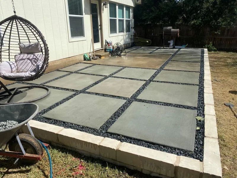 Concrete patio with square tiles, black gravel, and a hanging chair near a house.
