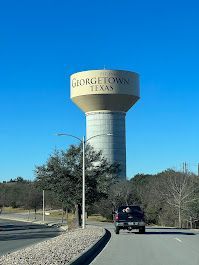 Georgetown, Texas water tower on a sunny day. A vehicle drives on a road in the foreground.