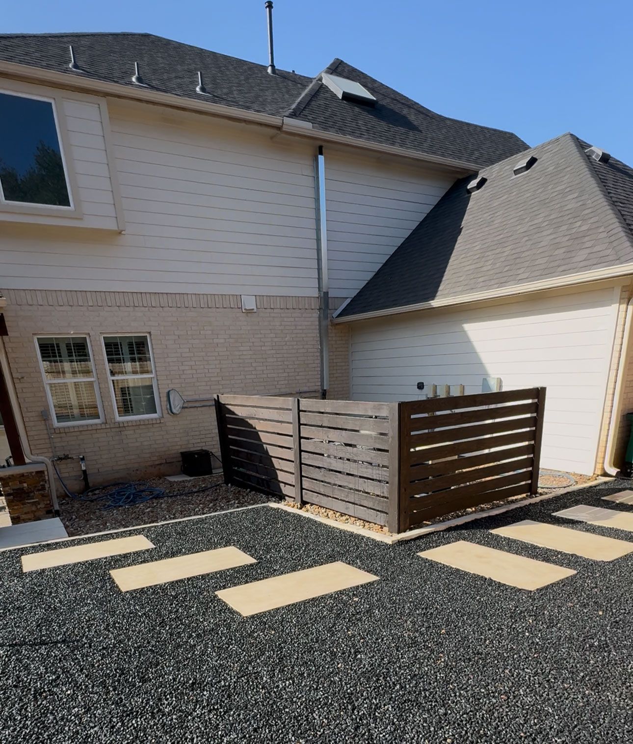 Backyard with beige house, dark gray gravel, stepping stones, and brown privacy fence.