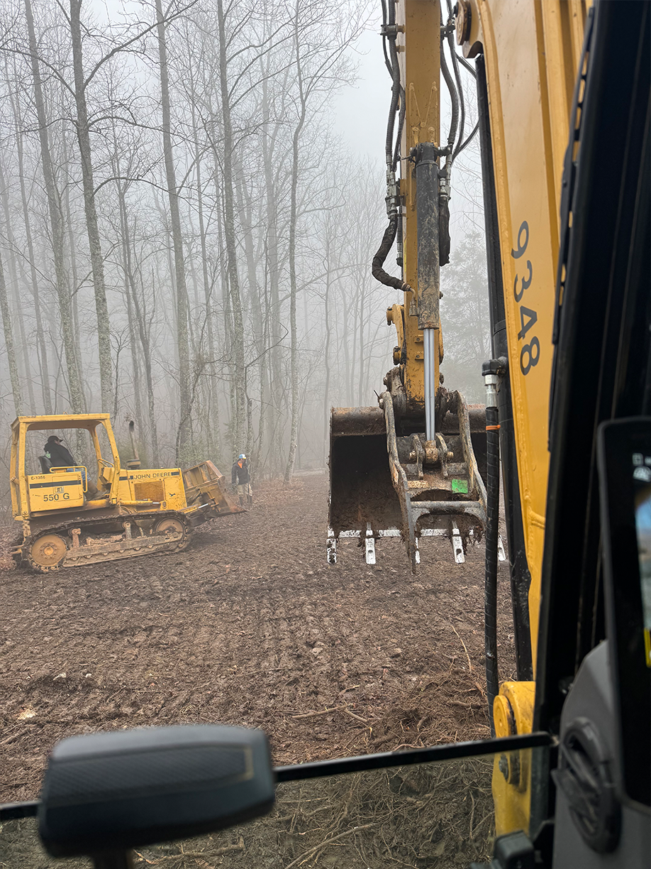 A yellow excavator is digging a hole in the middle of a forest.