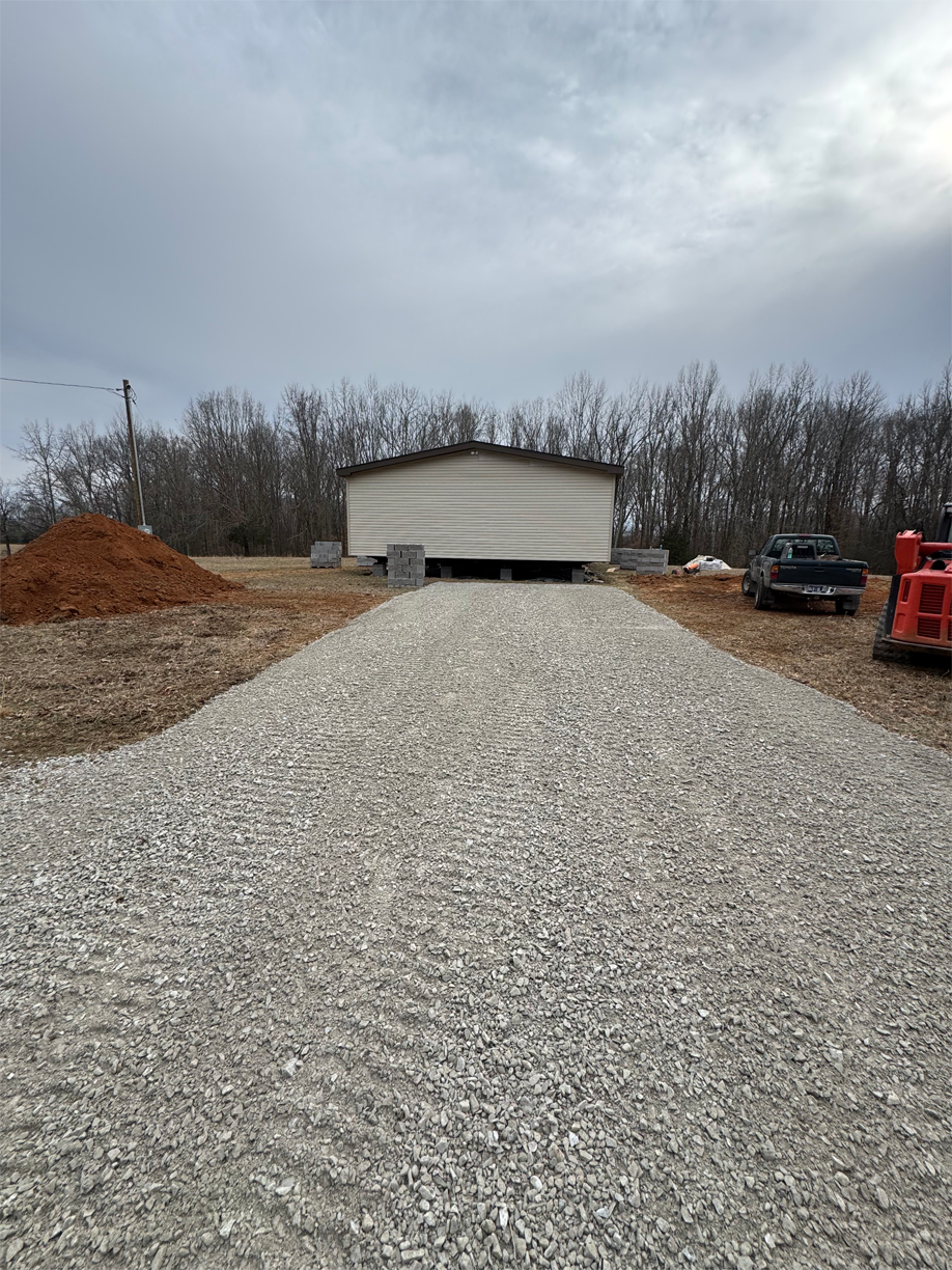 A gravel driveway leading to a house with a forklift in the background.