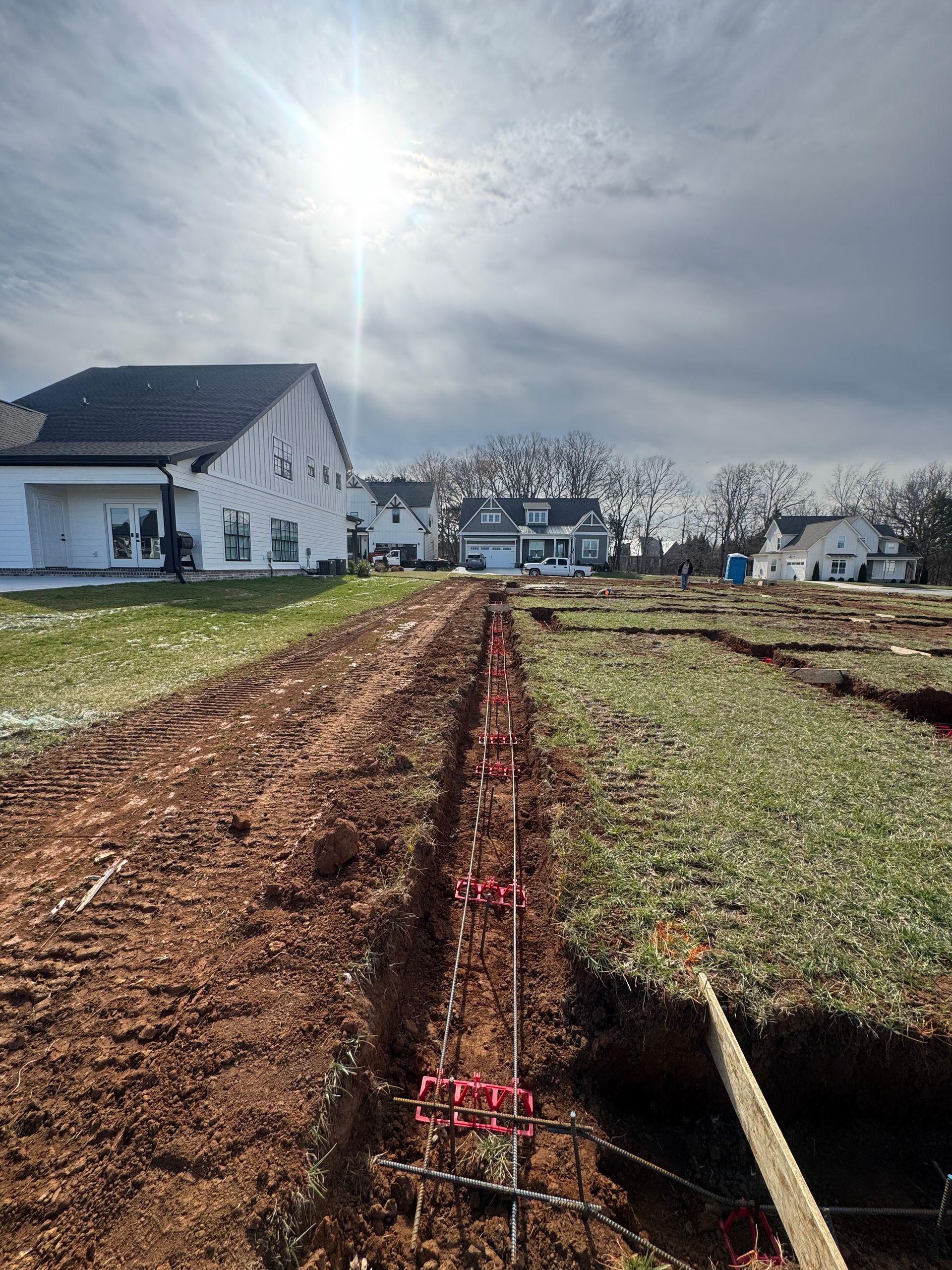 A dirt road going through a field with a house in the background.