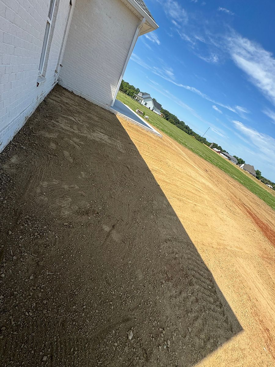 A shadow of a house is cast on a dirt road.