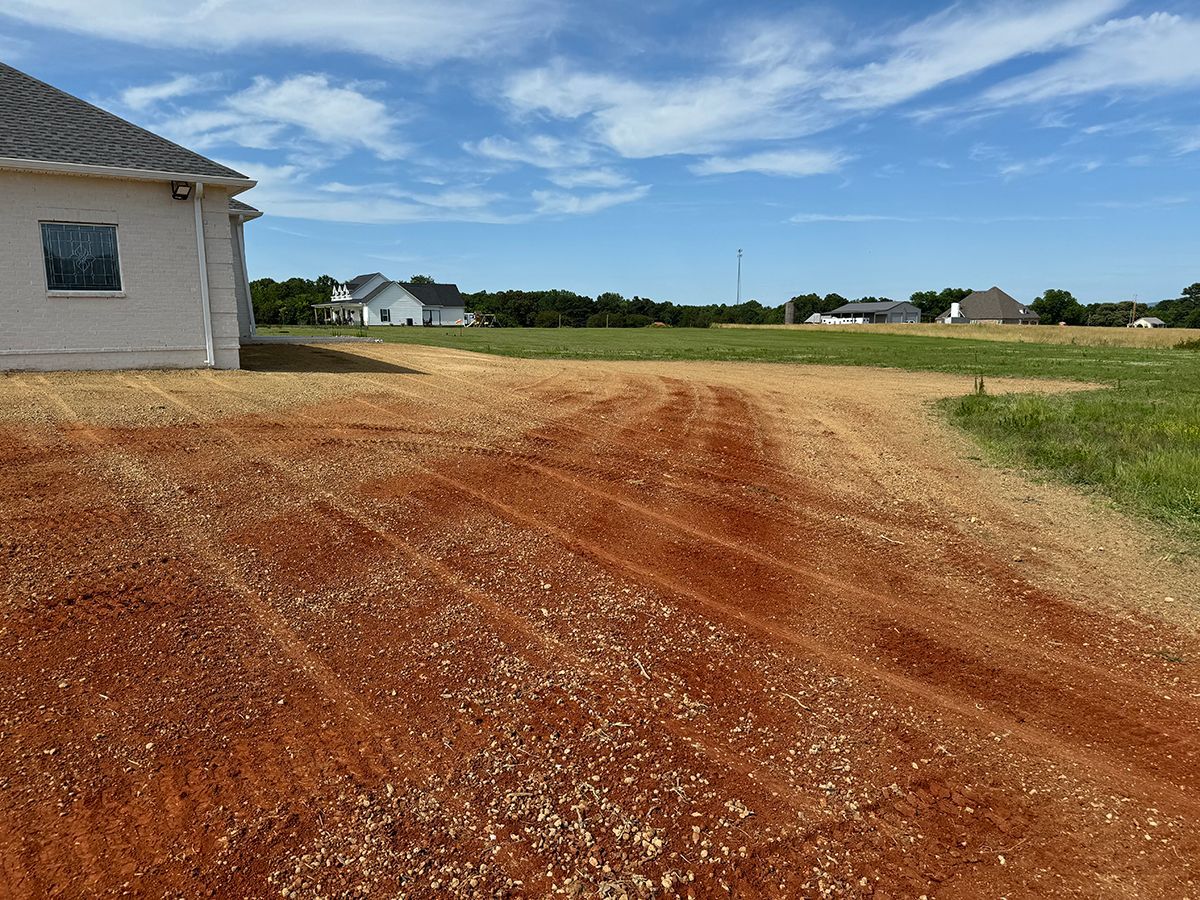 A dirt road leading to a house in a field.