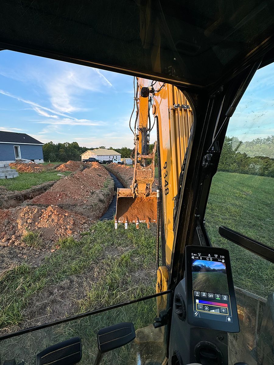 A person is driving a yellow excavator in a field.