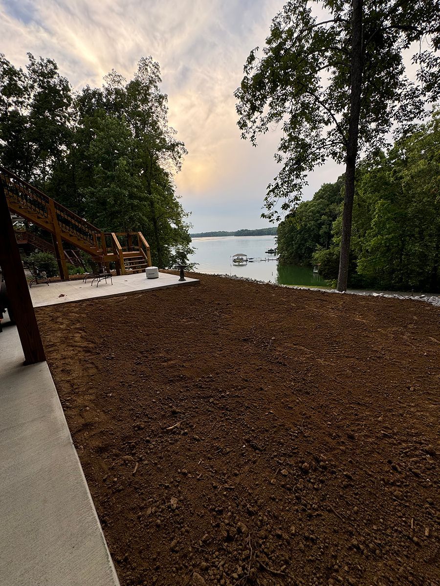 A large pile of dirt is sitting next to a body of water surrounded by trees.
