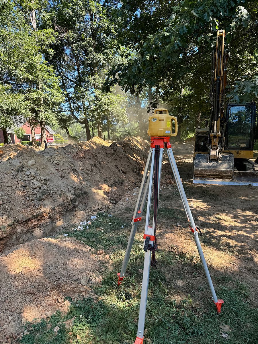 A tripod is sitting in the grass in front of a pile of dirt.