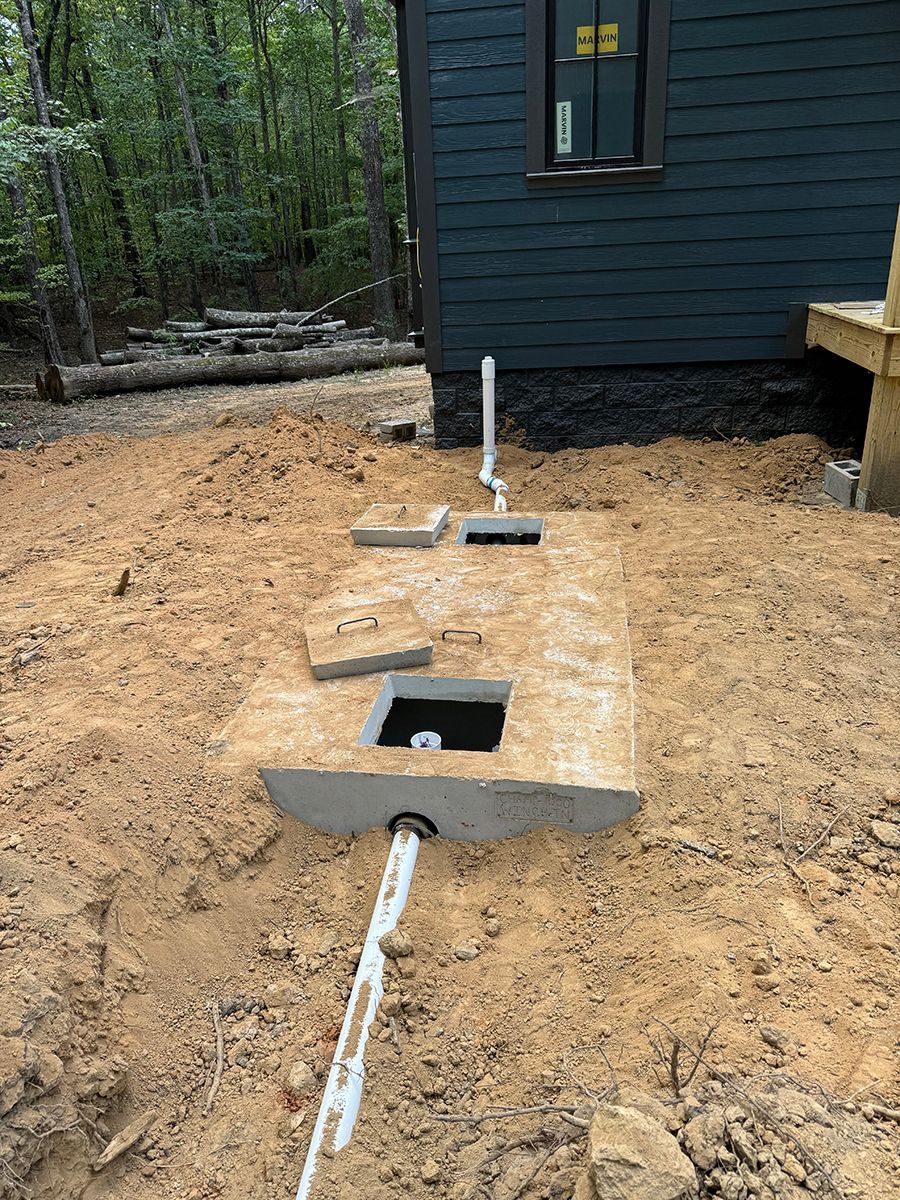 A septic tank is being installed in the dirt in front of a house.